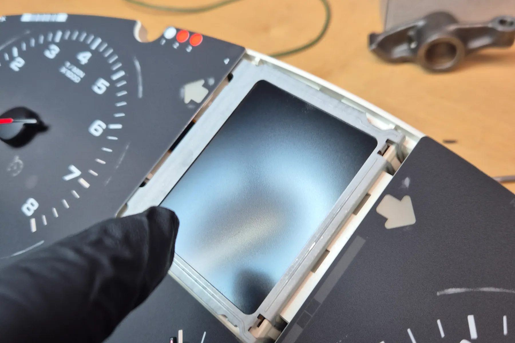 En behandsket hånd holder den adskilte instrumentenhed under reparation på værkstedsbordet